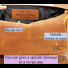 Brown leather bag with personalized text and initials on a wooden surface