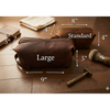Brown leather dopp kit with measurements on a wooden surface, including a razor and brush.