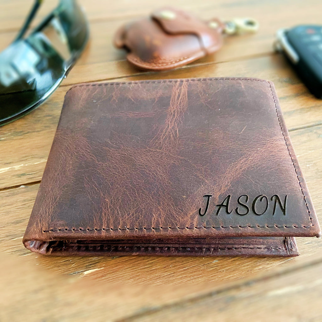 Brown leather wallet with 'JASON' engraving on a wooden surface.
