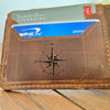 Brown leather cardholder with compass design holding cards on a wooden surface