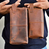 Two brown leather pouches held by a person against a neutral background