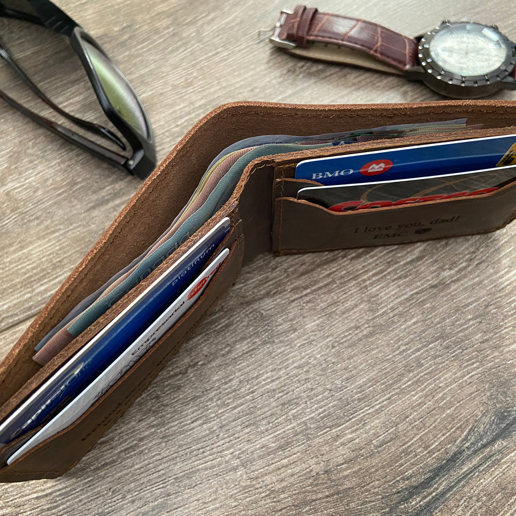 Brown leather wallet with cards on a wooden surface, accompanied by sunglasses and a watch.