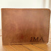 Brown leather wallet with 'JMA' initials on a wooden surface