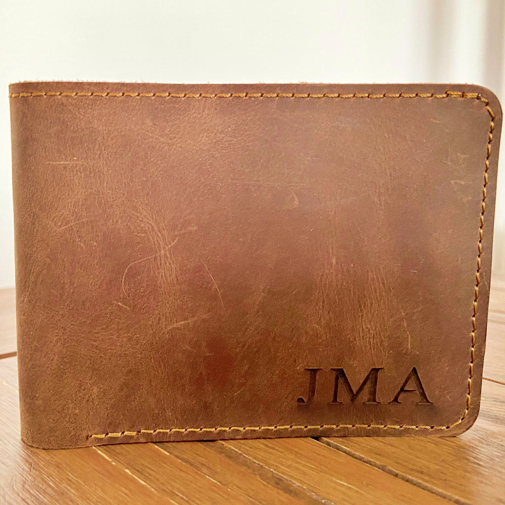 Brown leather wallet with 'JMA' initials on a wooden surface